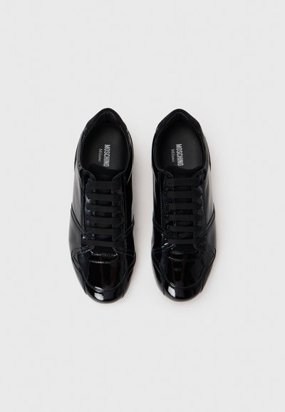 Black patent leather sneakers with a rounded toe, lace-up front, and smooth texture. Features minimalist design with subtle stitching details.