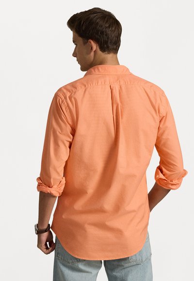 Oranssi pitkähiha sekä paita, jossa on napitettava kaulus, käärityt hihat ja takasivu, valmistettu sileästä kankaasta. Rennon muotoinen, huoliteltu helma.