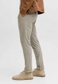Beżowe chinosy o slim fit, z bocznymi kieszeniami i podwiniętymi mankietami, w połączeniu z tanowymi zamszowymi botkami za kostkę. Gładka tekstura, klasyczny design.