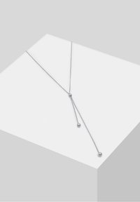 Collier délicat en argent en forme de Y avec deux chaînes pendantes, chacune se terminant par une petite perle en argent, présenté sur un bloc blanc.