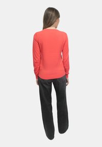 Maglione a maniche lunghe in maglia corallo, stile aderente, indossato con pantaloni neri larghi. Texture liscia, design semplice, senza pattern o dettagli visibili.