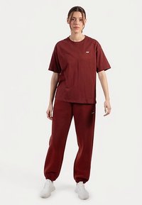 Burgundy t-shirt med avslappnad passform och joggers i bomullsblandning, med en diskret logga på tröjan. Mjuk textur, elastiska muddar på byxorna.