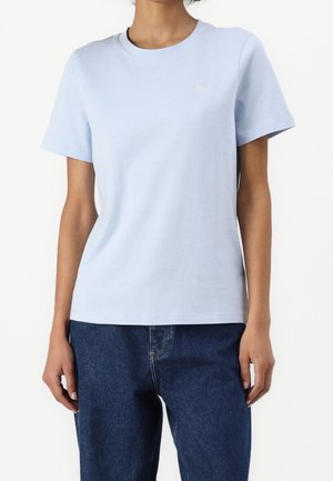 Person wearing a plain light blue short-sleeve t-shirt and dark blue jeans, standing against a white background.