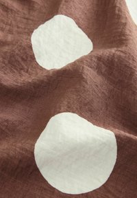 Tissu en lin marron avec des pois blancs irréguliers, présentant une surface texturée et un drapé doux. Idéal pour le textile et la décoration d'intérieur.