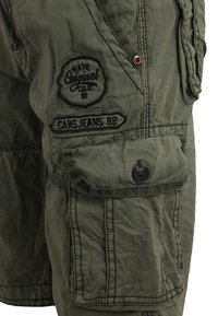 Shorts cargo verdi oliva in tessuto misto cotone. Le caratteristiche includono una tasca frontale con bottone, dettagli cuciti e patch con logo.