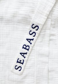 Witte bovenkleding gemaakt van gestructureerde stof met een ruitpatroon; beschikt over een blauw geborduurd "SEABASS" label op de strik.