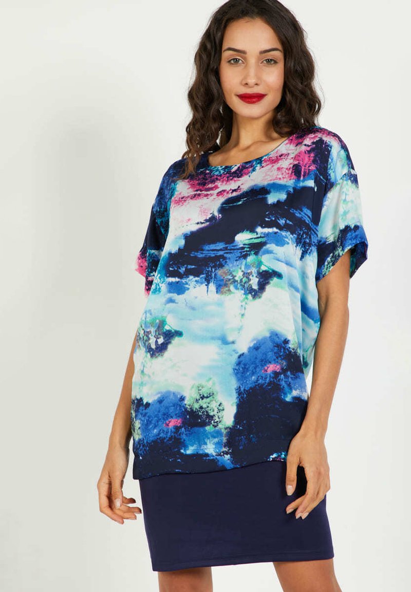 Top de mangas cortas multicolor en azul, rosa y verde con un patrón abstracto; tejido ligero con un corte holgado, combinado con una falda oscura.