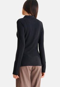 Zwarte ribbelige top met lange mouwen en een kraag, nauwsluitend ontwerp en verlengde mouwmanchetten, gecombineerd met beige wijde broek.