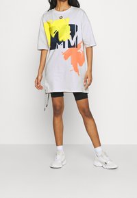 Šedé oversized tričko šaty s abstraktními vzory v žluté a oranžové barvě a námořnickým logem. Disponují kulatým výstřihem a bočními detaily.