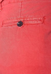 Röd tyg med en strukturerad finish, med en liten ficka med en svart knappdetalj. Sydda kanter och slät yta.