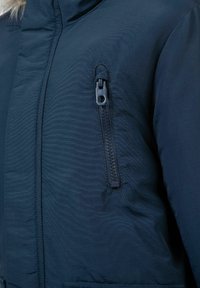Navy puffer jacket featuring a zippered pocket on the arm, made of textured fabric with a smooth finish, and a stand-up collar.