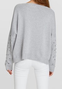 Pull gris oversize à manches longues avec des ornements, un col large et un ourlet arrière légèrement raccourci.