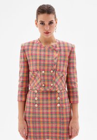 Pink and yellow checkered tweed jacket with three-quarter sleeves, a fitted silhouette, pockets, and large button details.