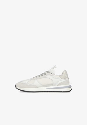 Zapatilla baja beige y blanca con paneles de malla y ante, cordones grises y suela blanca con banda de rodadura negra.