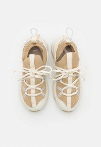 Beżowe i kremowe trampki z teksturowaną siateczką, kontrastującymi sznurowadłami i pętelką przy pięcie. Okrągły czubek i amortyzowana podeszwa.