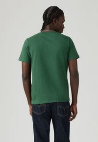 Tricou din bumbac verde, cu mânecă scurtă, guler rotund, design simplu, purtat cu blugi închiși la culoare cu un stil clasic cu cinci buzunare.