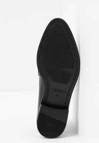 Semelle de chaussure en cuir noir avec une finition lisse, forme arrondie et motif de semelle subtil. Nom de marque gravé "Vagabond" et taille "37" visibles.