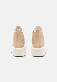 Botines de piel beige hasta el tobillo con una suela de goma blanca, que presentan un logo circular en la parte posterior y una lengüeta para ponerlos con facilidad. Textura suave.