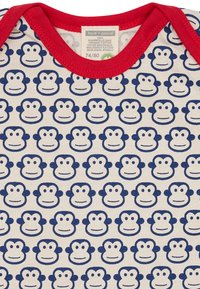 Weißer Bio-Baumwollstrampler mit rotem Ausschnitt, der mit einem sich wiederholenden Muster von blauen Affengesichtern versehen ist. Größenetikett: 74/80.