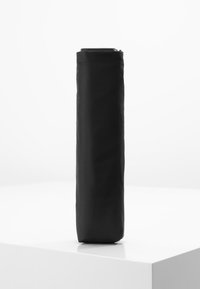 Custodia verticale nera realizzata in tessuto liscio, con chiusura a zip sulla parte superiore e forma cilindrica. Design minimalista.