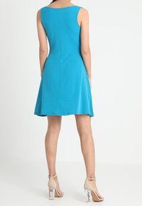 A sleeveless, knee-length dress in bright blue, made of smooth fabric with a fitted bodice, flaring skirt, and a central back seam.