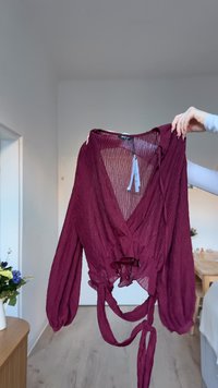 Burgundy, lightweight blouse with a crinkled texture, V-neckline, long puff sleeves, and a tie detail at the waist. Fabric has a flowy drape.