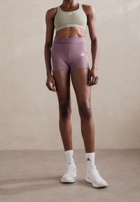 Grön sportbehå och lila träningsshorts med vita detaljer. Bärs med vita sportstrumpor och skor. Mjukt tyg, kroppsformad design.