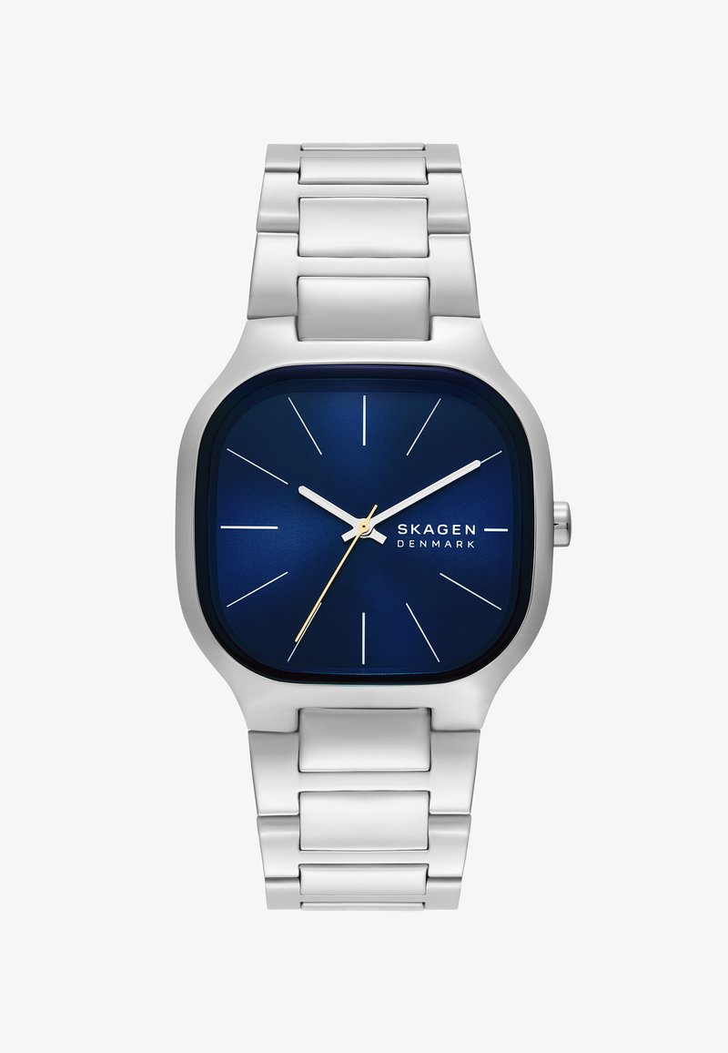 Ezüst rozsdamentes acél óra négyzet alakú tokkal és kék számlappal. Arany órás mutatóval, ezüst órakészítőkkel és polírozott fémszíjjal rendelkezik.