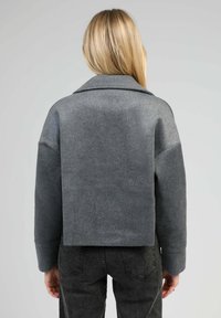 Veste courte en mélange de laine grise avec un large col, des épaules tombantes et des manches longues. Présente une texture douce et un design minimaliste.