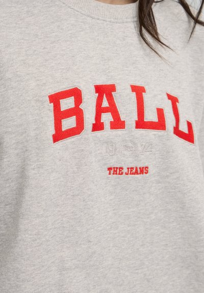 Pilkas džemperis su apvalia iškirpte, papuoštas ryškiai raudonais siuviniais "BALL" ir "THE JEANS", taip pat su metais "1974" mažesnėmis raidėmis.