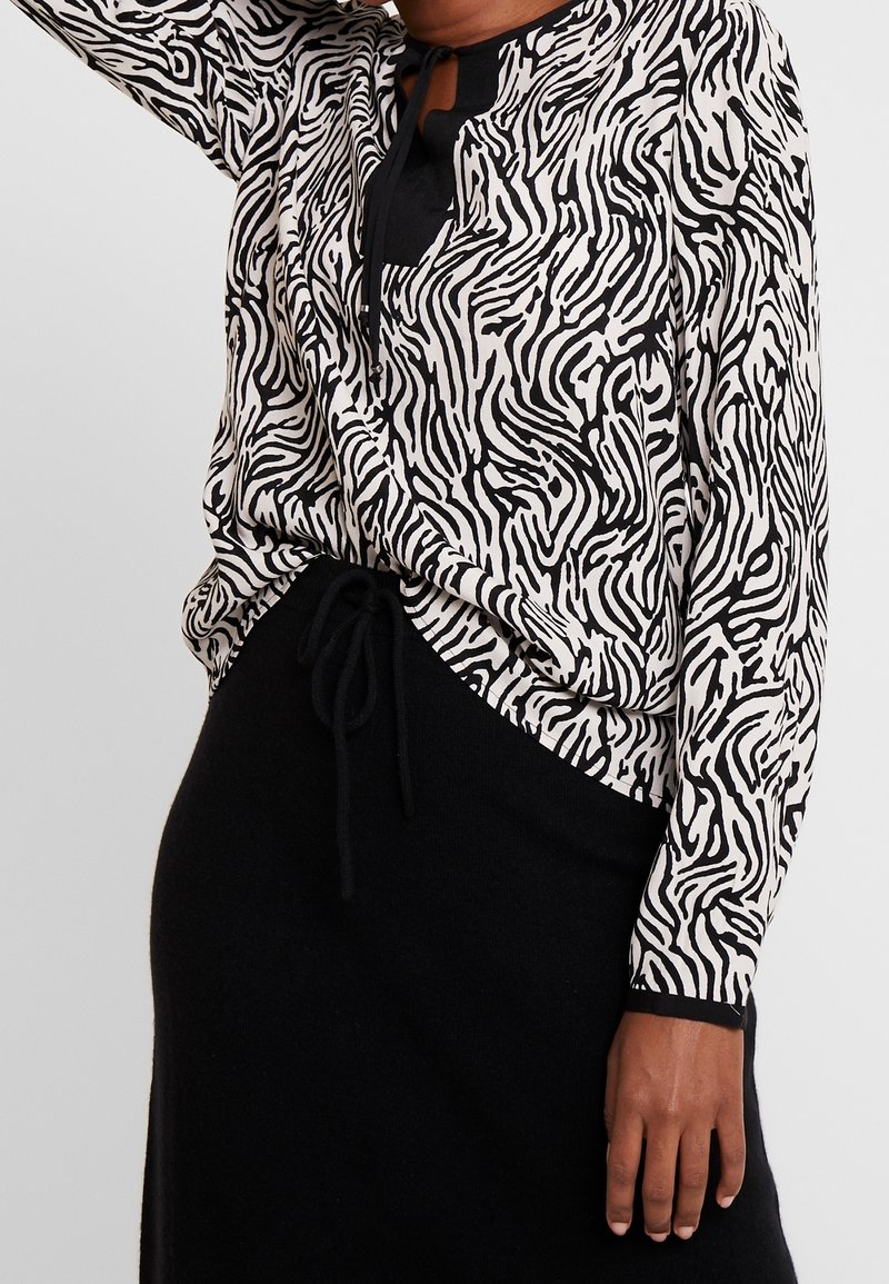 Top a righe bianche e nere con stampa zebra, scollatura rotonda e maniche lunghe, abbinato a una gonna nera con coulisse.
