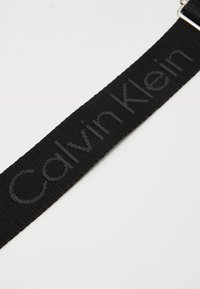 Black fabric belt with subtle Calvin Klein logo woven into the material and a silver metal buckle on a white background.