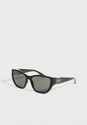 Gafas de sol negras con forma de ojo de gato con lentes oscuras y logo doble G dorado en las patillas, mostradas sobre fondo blanco.