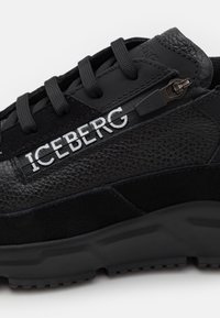 Svarta sneakers med en texturerad läderöverdel, släta accenter, svarta snören och en sidodragkedja har varumärket "ICEBERG" i vita bokstäver.