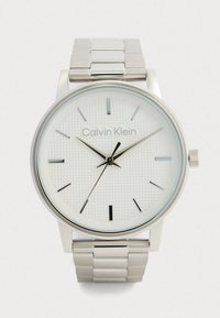 Montre-bracelet en métal argenté Calvin Klein avec un cadran blanc texturé, des index horaires minimalistes et trois aiguilles noires indiquant 10h10m35s.