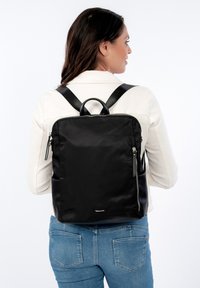 Black nylon backpack with smooth texture, rectangular shape, top handle, and adjustable shoulder straps; features a zipper and logo detail.