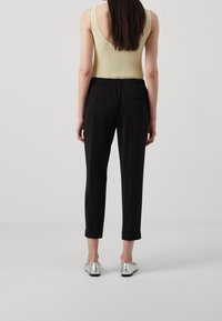 Body sans manches en jersey côtelé de couleur jaune clair, associé à un pantalon noir ajusté avec une taille élastique et des ourlets roulés. Chaussures argentées à enfiler.