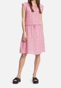 Robe à motif floral avec des manches courtes, taille élastique et ourlet jusqu'aux genoux dans des teintes de rose, jaune et blanc. Chaussures : sandales noires.