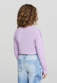 Długi rękaw, jasnofioletowa bluzka z okrągłym dekoltem, zestawiona z jasnoniebieskimi, luźnymi dżinsami z kieszeniami nakładanymi i wyblakłą fakturą.