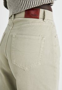 Beesvärvilised denim teksad tekstuurse viimistlusega, millel on nahast tagakülje silt "Papa Jeans" logo ja kaks tagakotit.
