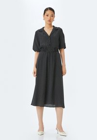 Musta pilkullinen midi-mekko, jossa on kauluspäänti, lyhyet puff-hihat ja elastinen vyötärö, valmistettu kevyestä kankaasta.