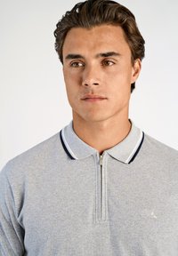 Grå zip-up polo t-shirt med texturerad finish; har en marinblå kant på kragen och en liten broderad logotyp på bröstet.