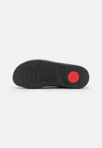 Crna gumena srednja podrška s teksturiranom površinom, koja ističe "fitflop" logo. Na jednoj strani se nalazi crveni kružni naglasak.