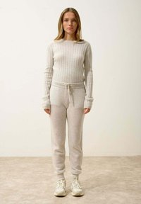 Svetle šedý pletený svetr s ribovanou texturou a dlouhými rukávy, doplněný o odpovídající jogger kalhoty s elastickým pasem a tkaničkou.
