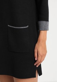 Abito nero in maglia con polsini e rifinitura pocket grigi. Presenta una fessura laterale e una vestibilità casual, mettendo in mostra un tessuto strutturato.