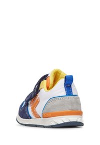 Sneaker blu e bianco con cinturino in velcro, dettagli grigi e arancioni, rivestimento giallo e materiale testurizzato in un design sportivo.