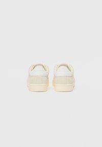 Sneakers bianchi in suede con retro in pelle liscia. Silhouette arrotondata, suola in gomma crema e design minimalista. Nessun marchio visibile.