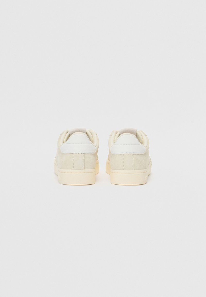 Białe zamszowe sneakersy z gładkim skórzanym tyłem. Zaokrąglony fason, kremowa gumowa podeszwa oraz minimalistyczny design. Brak widocznych logo.