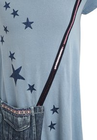 Jasnoniebieski top z ciemnoniebieskimi nadrukami gwiazdek, z deninową kieszonką. Regulowane ramiączka z różowymi cekinami na brzegach. Miękki, swobodny materiał.