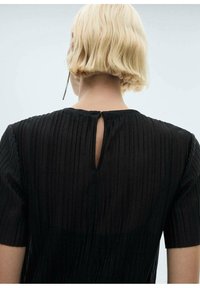 Črna obleka s kratkimi rokavi, ki ima vertikalne gubice, detajl s ključavnico na zadnji strani in lahek material.